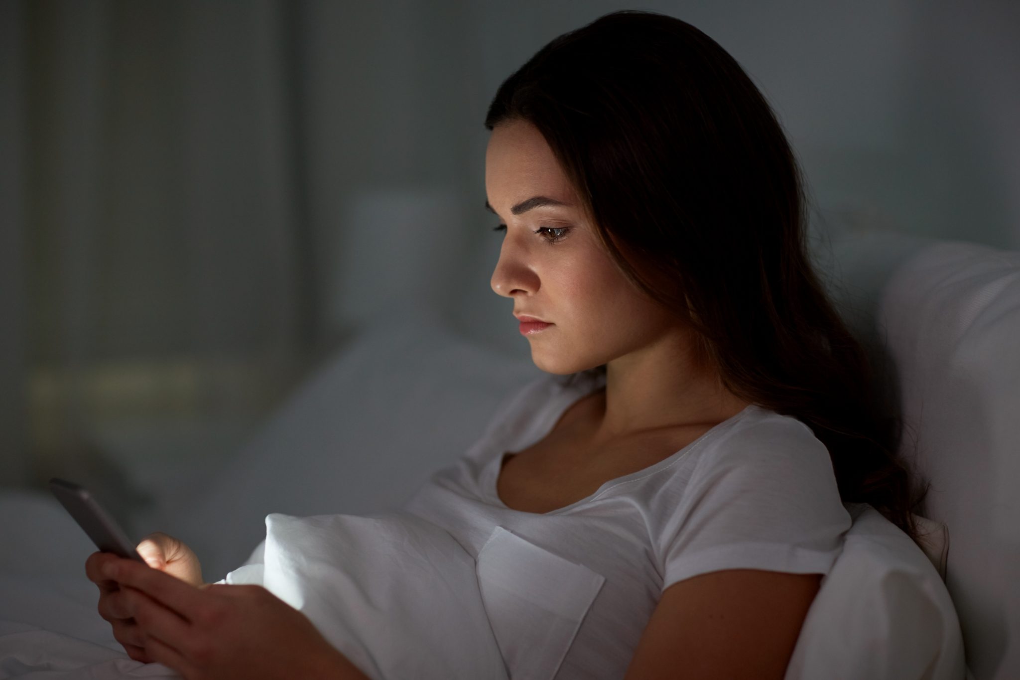 young woman with smartphone in bed at night